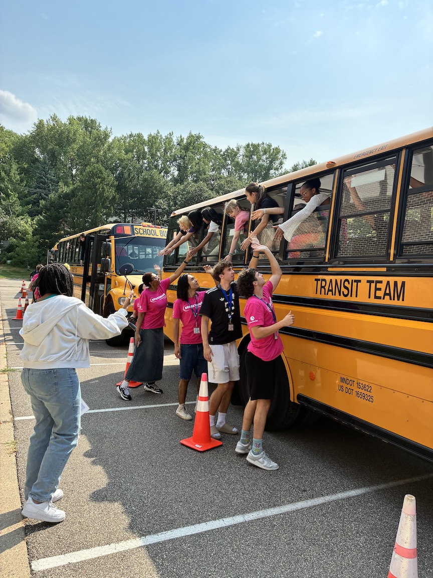 Photo of students on a yellow school bus giving high fives to teachers outside of the bus.